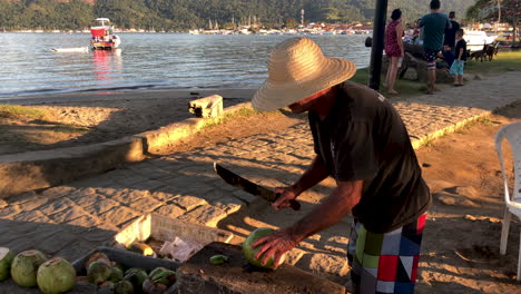 Brazilian-man-carving-melon,-the-small-harbor-is-visible-in-the-background