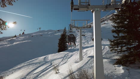 A-young-couple-riding-a-chair-lift-through-snow-covered-alpine-trees-Montafon-Ski-Arena-Austria,-slow-motion