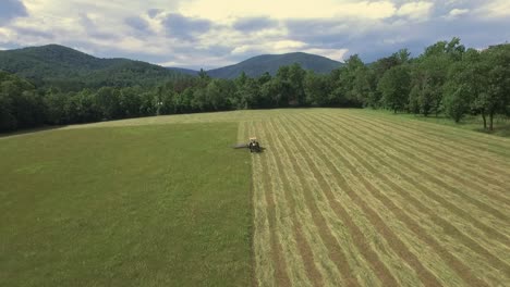 Aerial-tilt-down,-up-of-farmer-cutting-hay-with-tractor-during-harvest