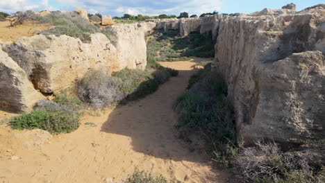 A-pathway-through-ancient-ruins-at-the-Tombs-of-the-Kings-in-Pafos,-Cyprus,-surrounded-by-rocky-walls