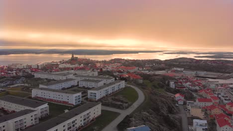 Flying-over-the-peaceful-city-of-Lysekil,-Sweden-with-the-fiery-orange-sunset-in-the-horizon---Aerial-shot