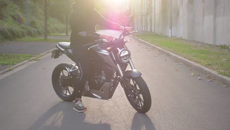 Motorradfahrer-Setzt-Seinen-Helm-Auf-Und-Setzt-Sich-Auf-Sein-Motorrad,-Um-Bei-Sonnenuntergang-Eine-Fahrt-Zu-Unternehmen