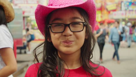 Asian-girl-with-cowboy-hat-making-a-funny-face-at-camera-in-a-carnival-fair-in-slow-motion-4K