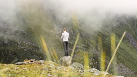 Camera-zooming-out:-Man-standing-on-a-small-rock-on-the-edge-of-a-cliff,-enjoying-and-photographing-scenic-view-of-cloudy-mountains