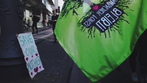 A-sign-reading-"Save-our-mother"-is-leaning-against-a-streetlight-whilst-climate-activists-march-past-to-protest-global-warming