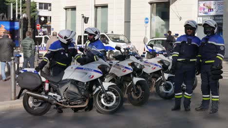 Four-police-officers-in-a-blue-uniform-and-wearing-helmets-gather-in-front-of-their-motorbike-parked-to-block-the-street-to-talk-to-each-other-before-the-beginning-of-the-demonstration