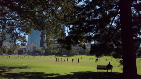 Ein-Männlicher-Büroangestellter-Schaut-Sich-Während-Der-Mittagspause-In-Einem-Park-Im-Schatten-Ein-Freundschaftsspiel-Im-Fußball-An