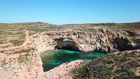 Eine-Faszinierende-Drohnenaufnahme-Von-Freunden,-Die-Auf-Einer-Klippe-In-Der-Blauen-Lagune-Auf-Der-Insel-Comino-Stehen