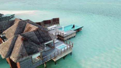 Aéreo,-Disparo-De-Drone,-Alrededor-De-Una-Mujer,-Caminando-En-La-Terraza,-En-Un-Bungalow-En-El-Mar,-En-Un-Día-Soleado,-En-La-Isla-Conrad-Rangoli,-En-Maldivas