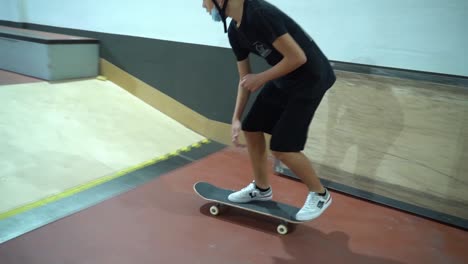 Un-Joven-Con-Máscara-Haciendo-Trucos-De-Patineta-360-Y-Moliendo-Sobre-Rieles-En-Un-Parque-De-Patinaje-Cubierto