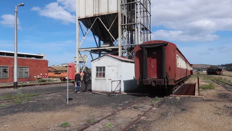 Two-teenage-boys-walk-behind-small-building-in-derelict-train-yard,-wide-shot-hand-held