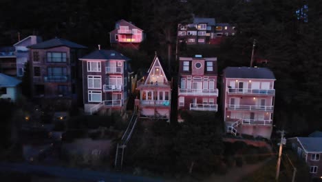 Drone-flies-backwards-away-from-couple-sitting-on-a-deck-of-an-A-frame-cabin-at-sunset