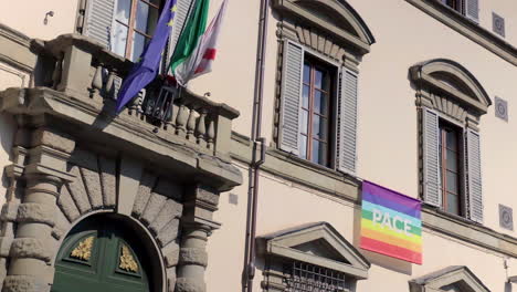 Vista-De-ángulo-Bajo-Del-Edificio-Con-Banderas-De-La-UE-Y-La-Paz-Ondeando-Suavemente-En-El-Viento,-Florencia