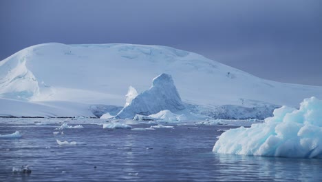 Global-Warming-in-Antarctica,-Warming-Oceans-with-Sunny-Sunshine-Sun-Shining-on-Icebergs-and-Ice-with-Mountains-Landscape-Scenery,-Ocean-and-Sea-Water-Warming-in-Antarctic-Peninsula-Winter-Scene