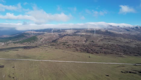 Beautiful-aerial-shot-of-Croatian-landscape-with-wind-turbines-generating-renewable-energy-in-the-background-and-an-empty-road,-in-the-region-of-Lika-in-Croatia,-Europe