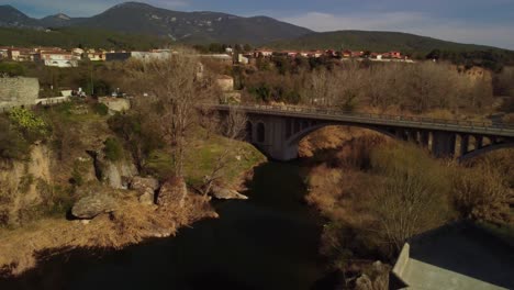 Medieval-stone-bridge-over-a-river-in-Besalú,-Girona-with-scenic-mountains-in-the-background
