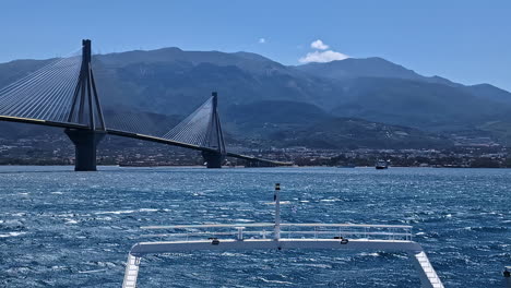 Panorama-Der-Rio-Antirrio-Brücke-überquert-Das-Blaue-Griechische-Meer,-Golf-Von-Korinth,-Aufnahme-Eines-Motorboots,-Das-Griechenland-Unter-Der-Sonne-Segelt