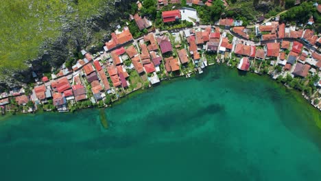 Red-Roofed-Houses-by-the-Emerald-Lake:-Drone-View-of-the-Serene-Touristic-Village-Beneath-the-Beautiful-Rocky-Peninsula-in-Lin,-Pogradec