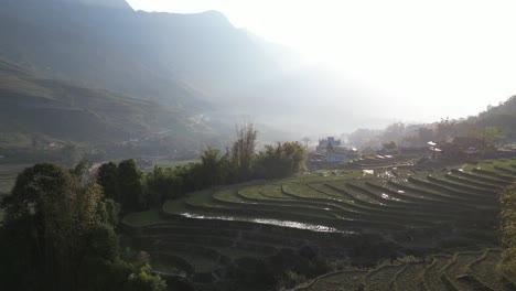 Aerial-drone-shot-of-hazy-sunrise-above-bright-green-rice-terraces-in-the-mountains-of-Sapa,-Vietnam