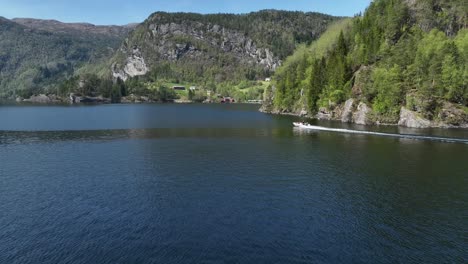 Side-view-of-a-RIB-speedboat-cruising-in-Bolstadfjord,-revealing-Tysseknappen-triple-waterfalls-behind-headland