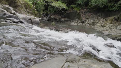 Waters-of-Goa-Rang-Reng-waterfall-in-Bali,-Indonesia,-cascading-over-smooth-rocks-and-surrounded-by-lush-greenery