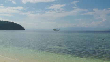 A-distant-sailboat-rests-anchored-off-Kri-Island-in-Raja-Ampat,-Indonesia