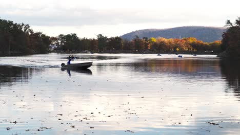 Man-In-A-Boat-Turning-Around-On-A-Lake-In-Autumn-With-A-Mountain-Behind-Him