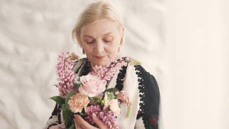 portrait-depicts-a-lovely-elderly-gray-haired-woman-in-authentic-embroidered-Ukrainian-attire-holding-a-beautiful-bouquet-of-flowers