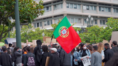 Porto---Portugal---june-6th-2020:-BLM-Black-Lives-Matter-Protests-Demonstration-with-protestor-carrying-Portuguese-flag-while-walking-into-the-protest