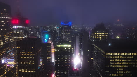 Drone-flying-parallel-to-skyscrapers-at-Times-square,-foggy-night-in-New-York,-USA