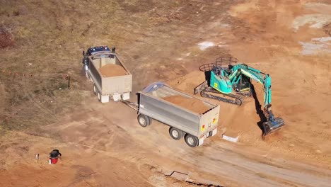 Truck-and-trailer-pulling-away-from-a-dirt-pile-after-being-loaded-by-a-tracked-excavator