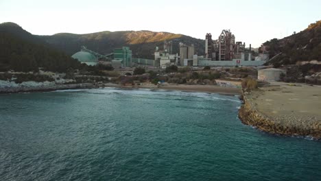 Costa-garraf-coastline-with-a-cement-factory-in-barcelona,-spain-at-sunset,-aerial-view