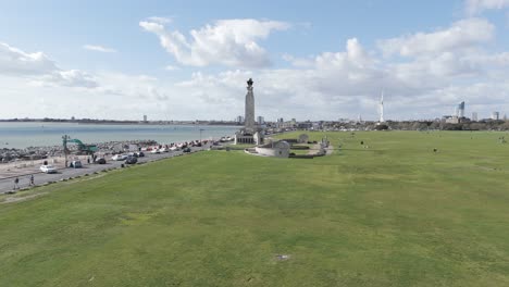 Drone-flight-from-a-distance-approaching-Navy-War-Memorial-Southsea-with-Southsea-Common-and-sea-front-and-views-towards-Portsmouth-docks-on-bright-sunny-day