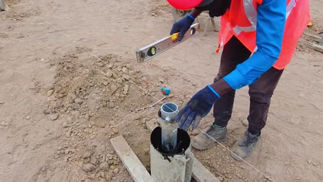 Trabajador-De-La-Construcción-Africano-Instalando-Y-Nivelando-El-Molde-Del-Marco-De-Pilotes-De-Concreto-Y-Soporte-Para-La-Instalación-De-Pilotes-De-Concreto-De-Granjas-Solares-Fotovoltaicas