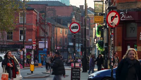 Bustling-street-scene-in-the-Northern-Quarter,-Manchester-with-cars,-pedestrians,-and-colorful-buildings