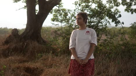 Woman-standing-in-a-field-at-sunset,-looking-up-and-touching-her-chest