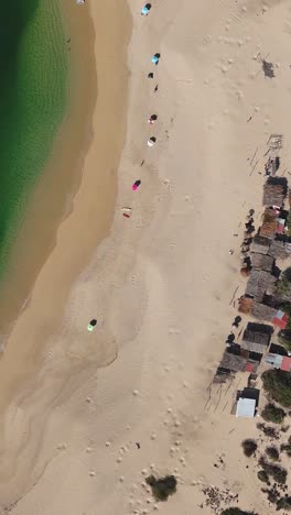 Beach-view-with-green-waters,-umbrellas,-and-small-houses-along-the-bay