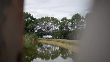 Silver-Stretch-Limousine-Drives-On-Dirt-Driveway-Next-To-A-Dam,-SLOW-MOTION