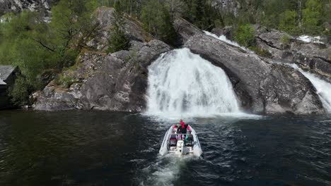 Aerial-following-tourist-on-RIB-safari-into-waterfall-at-Tysseknappen-Norway,-slow-motion