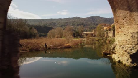 Antiguo-Puente-De-Piedra-En-Besalú,-España,-Reflejándose-En-Un-Río-Tranquilo-En-Un-Día-Soleado