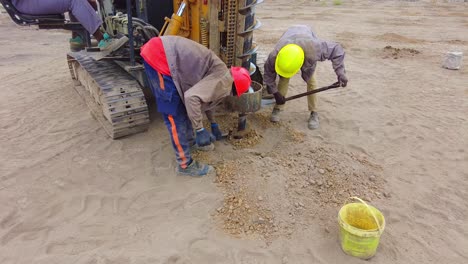 Construction-workers-labour-to-clear-dirt-after-pile-driver-digs-deep-hole-for-solar-PV-farm-foundation---Gambia,-West-Africa