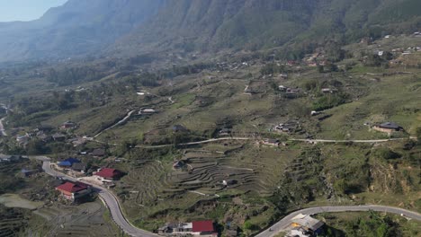 Aerial-drone-shot-of-road-leading-through-village-amidst-bright-green-rice-terraces-in-the-mountains-of-Sapa,-Vietnam