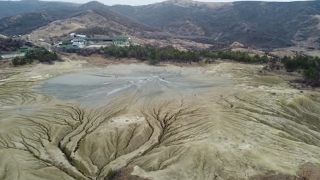 Perspectiva-Aérea-Del-Paisaje-Volcánico-De-Las-Montañas-De-Rumania-Con-Sus-Volcanes-De-Lodo,-Tierra-Seca-Con-Grietas,-Con-Algunas-Casas-Y-Pueblos-Aislados