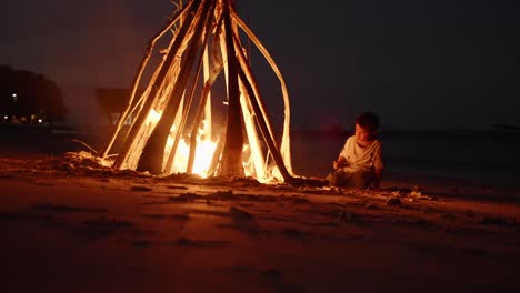 Boy-playing-with-Branch-at-Bonfire-under-Tropical-night-of-Komodo-Indonesia-Fire-burning-in-the-Dark