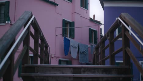 Wooden-bridge-leading-to-colorful-houses-with-laundry-hanging-on-Burano-Island,-Venice