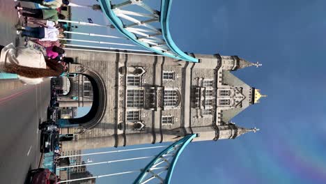 Vertical-view-of-Tower-Bridge,-bustling-with-road-traffic-and-pedestrians-on-sidewalks,-vibrant-sunny-daytime-scene