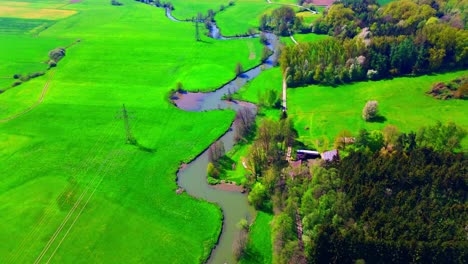 Vista-Aérea-Del-Río-Serpentino-Que-Fluye-A-Través-De-Campos-Verdes-Y-Bosques