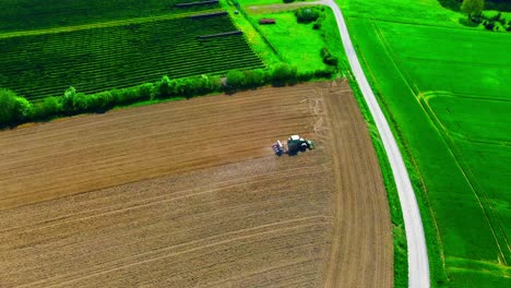 Luftaufnahme-Eines-Traktors,-Der-Ein-Feld-Neben-üppigem-Grünem-Ackerland-Und-Einer-Solarpanel-Farm-Pflügt
