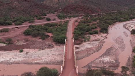 Un-Camino-De-Tierra-Roja-Y-Un-Puente-Que-Cruza-El-Lecho-De-Un-Río-Seco-En-La-Ruta-68,-Salta,-Argentina,-Vista-Aérea