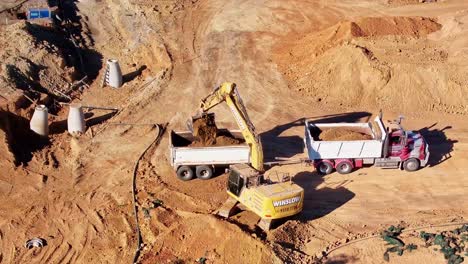 Truck-and-trailer-being-loaded-with-dirt-from-a-dirt-pile-by-a-tracked-excavator-at-a-new-construction-site